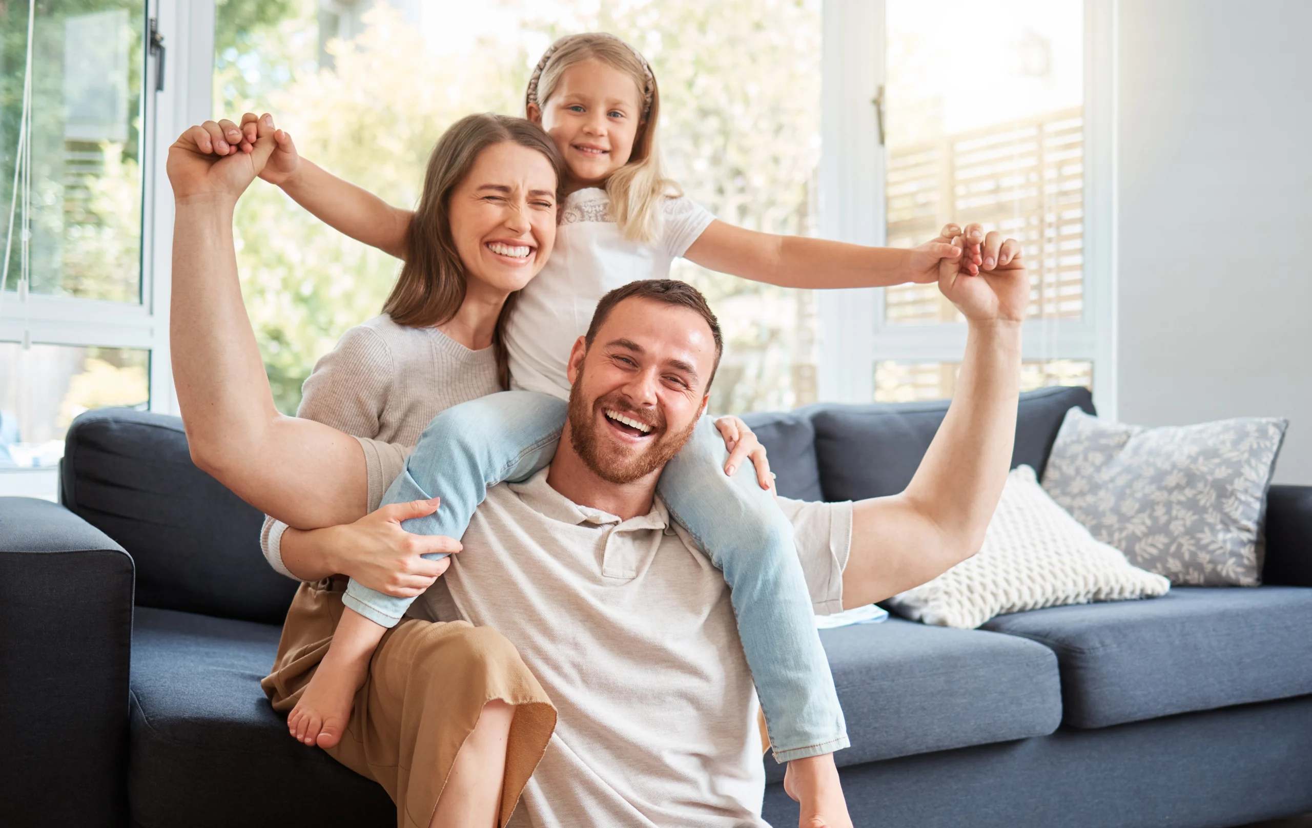 A father holds his daughter on his shoulder with his smiling wife behind them