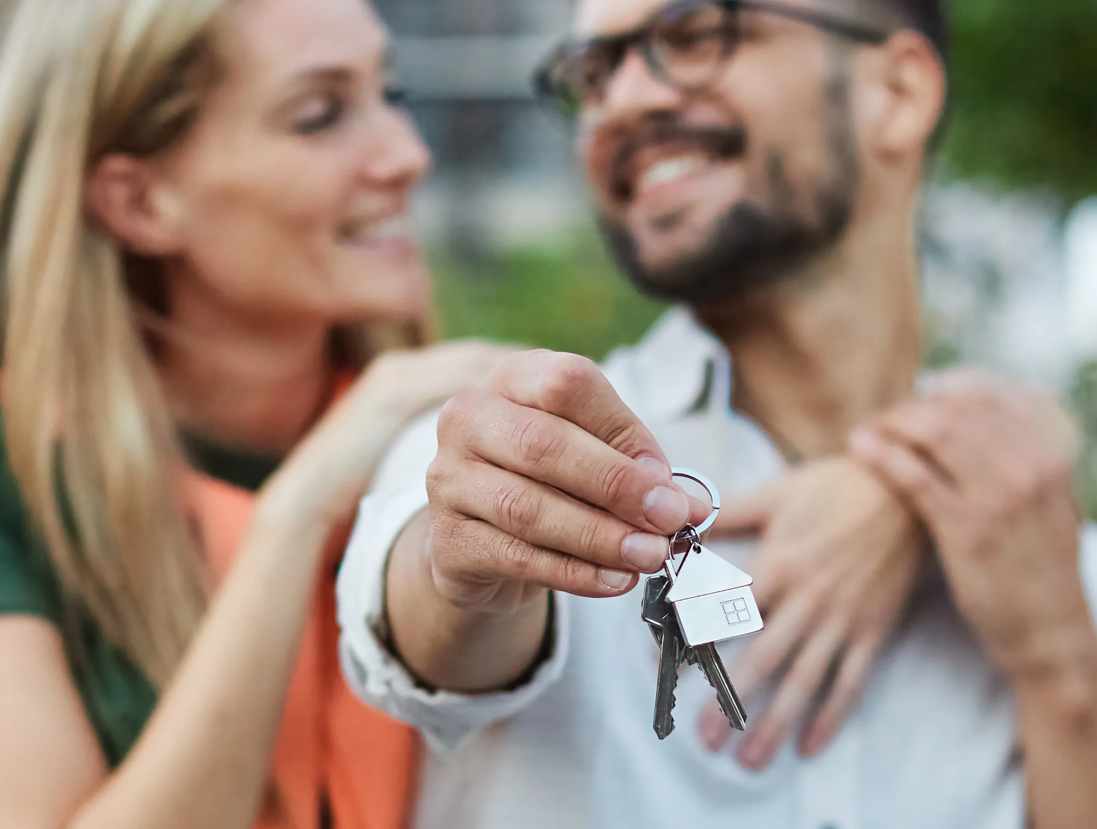 Husband and wife smile at each other while holding out keys to their new home