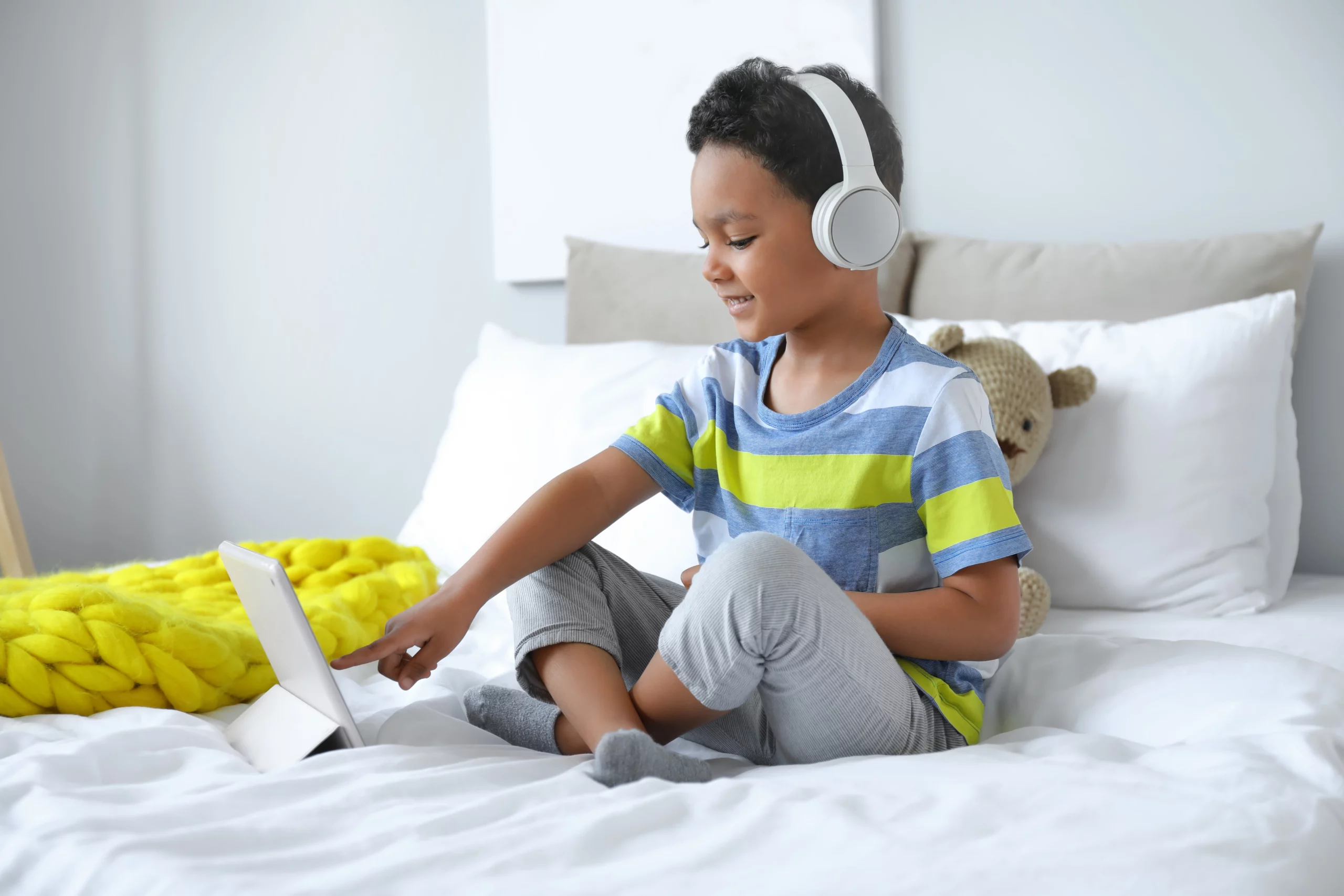 kid with headphones on watching videos on his iPad sitting on his bed