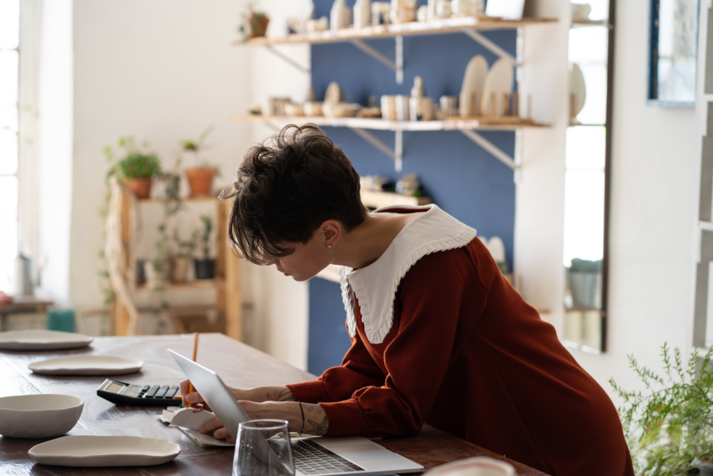 Person uses a laptop and calculator at home to review their finances