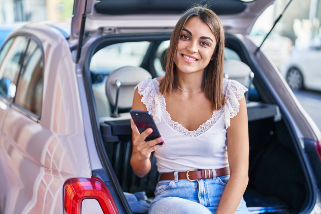 Woman sitting in the back of a car uses her phone to apply for a Swoosh emergency loan