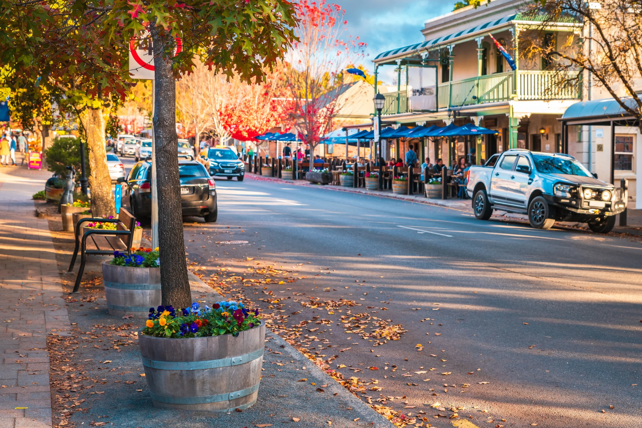 Vibrant street scene in Hahndorf, Adelaide Hills, with planters, parked cars, and historic buildings with outdoor seating.
