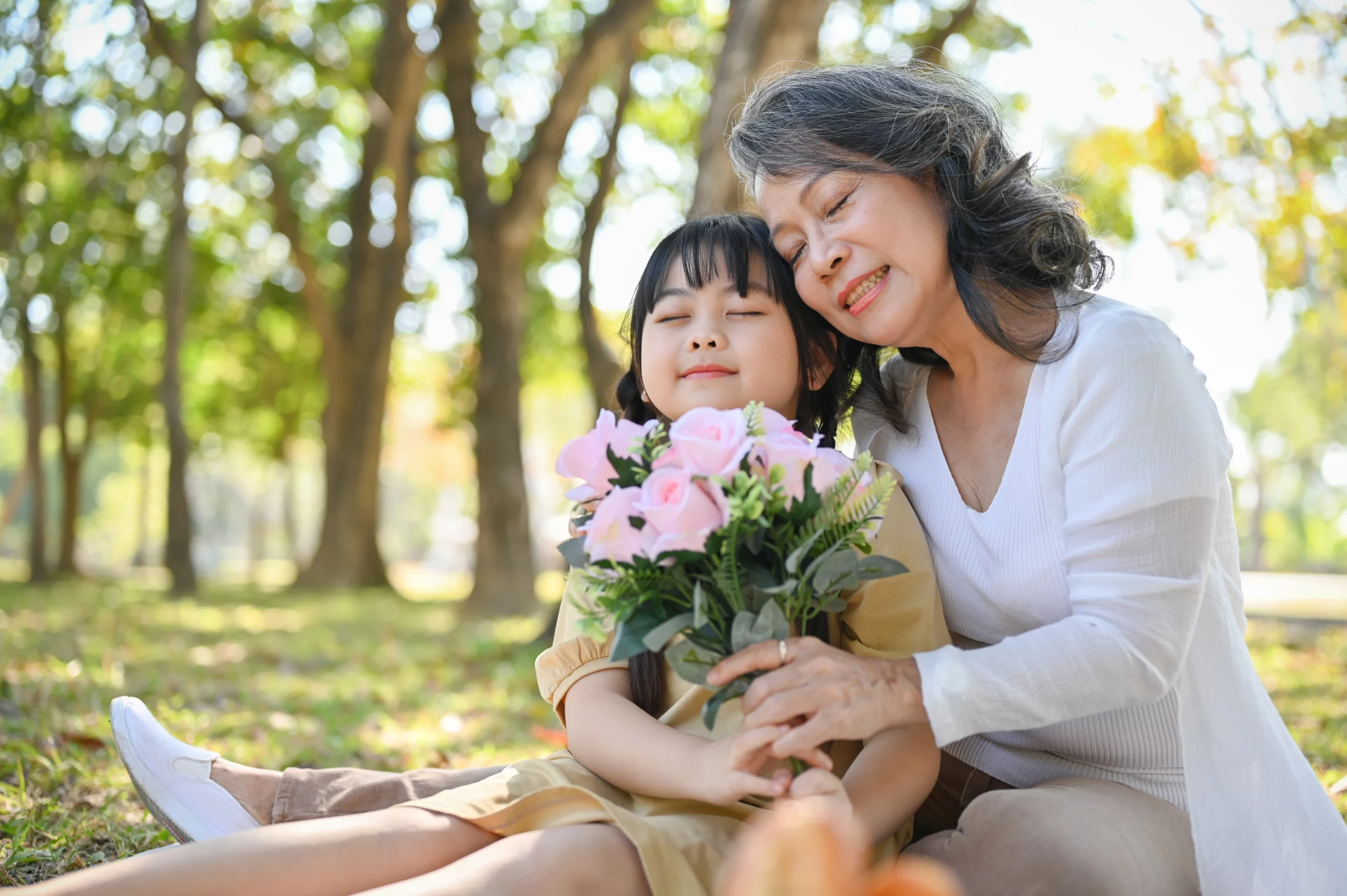 mother and daughter hugging with eyes closed in a park with a bouquet of light pink roses