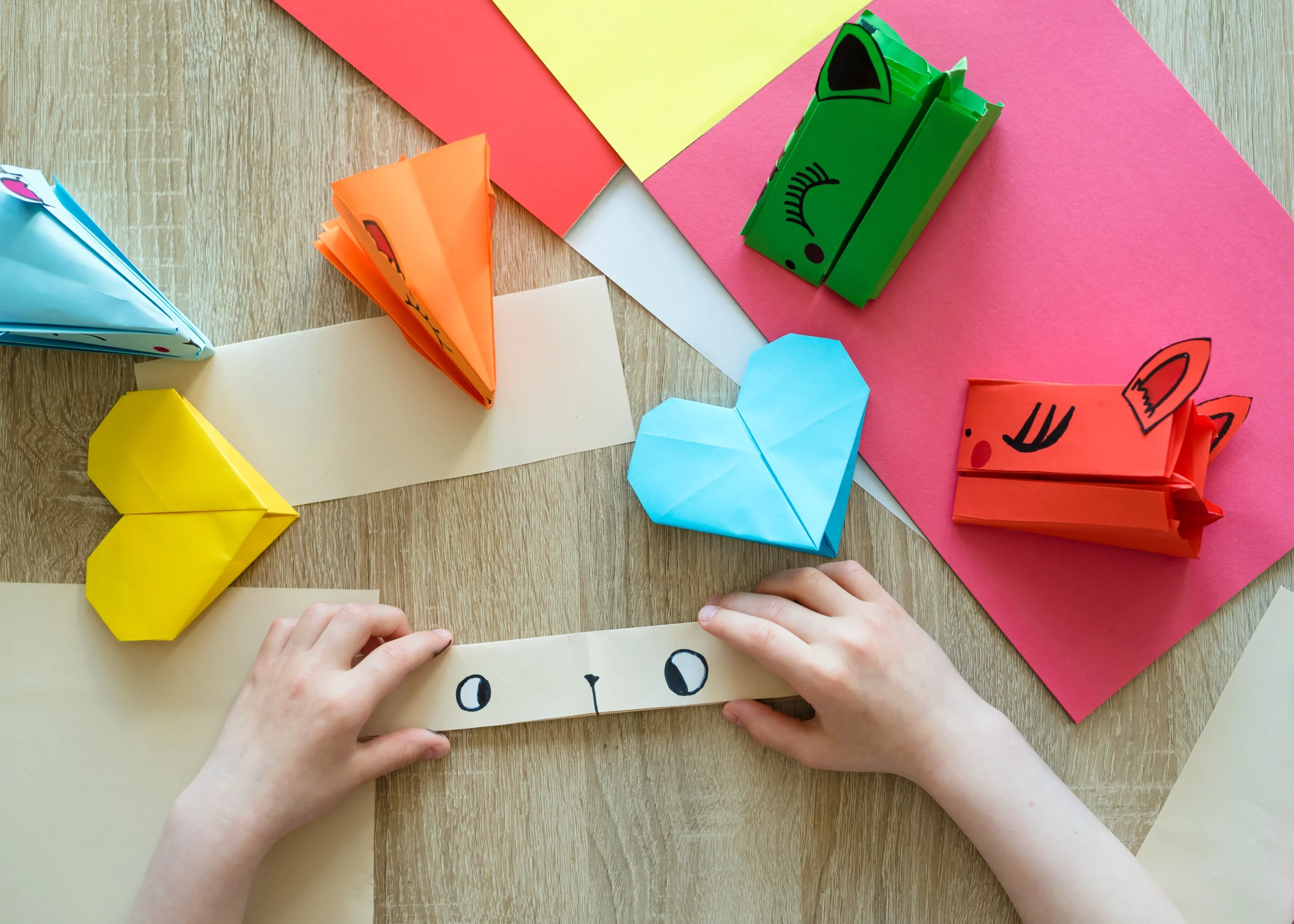 paper and origami hearts and animals laid out on a table with child's hands folding up another animal