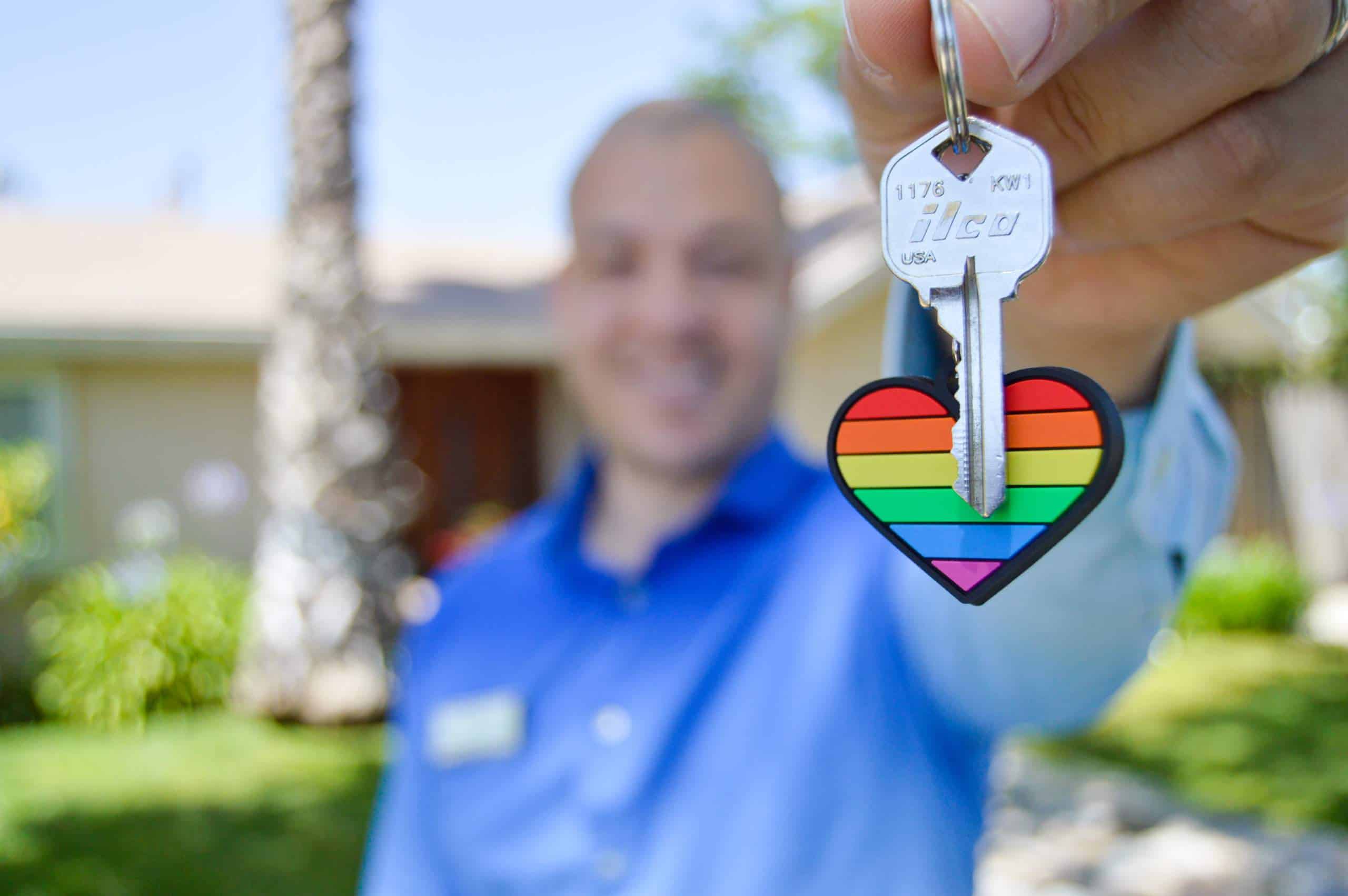 man holding up keys to a new house with a rainbow loveheart keyring