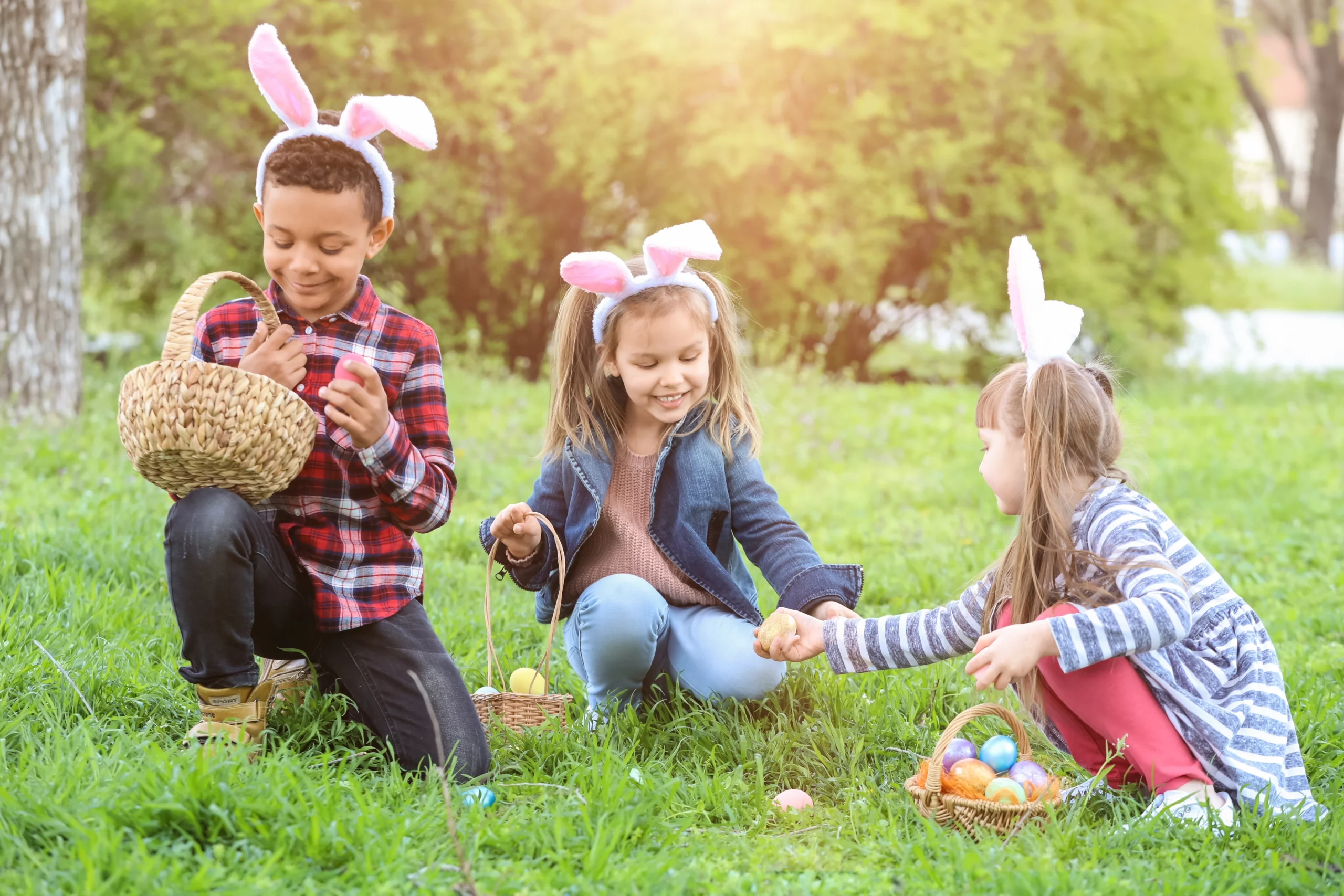 children wearing bunny ears holding Easter baskets on an Easter egg hunt in a park