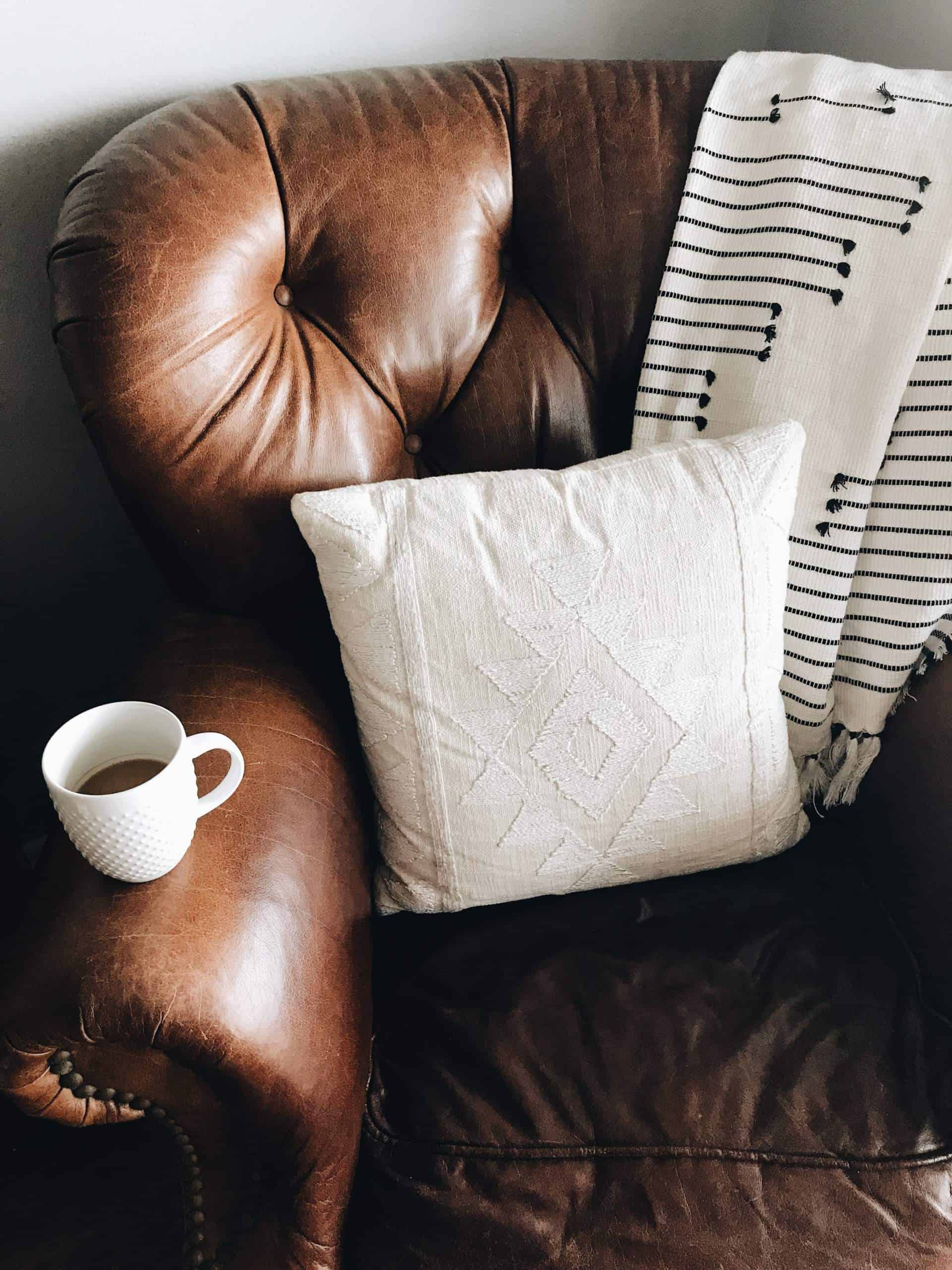 brown leather couch with coffee mug white pillow and blanket