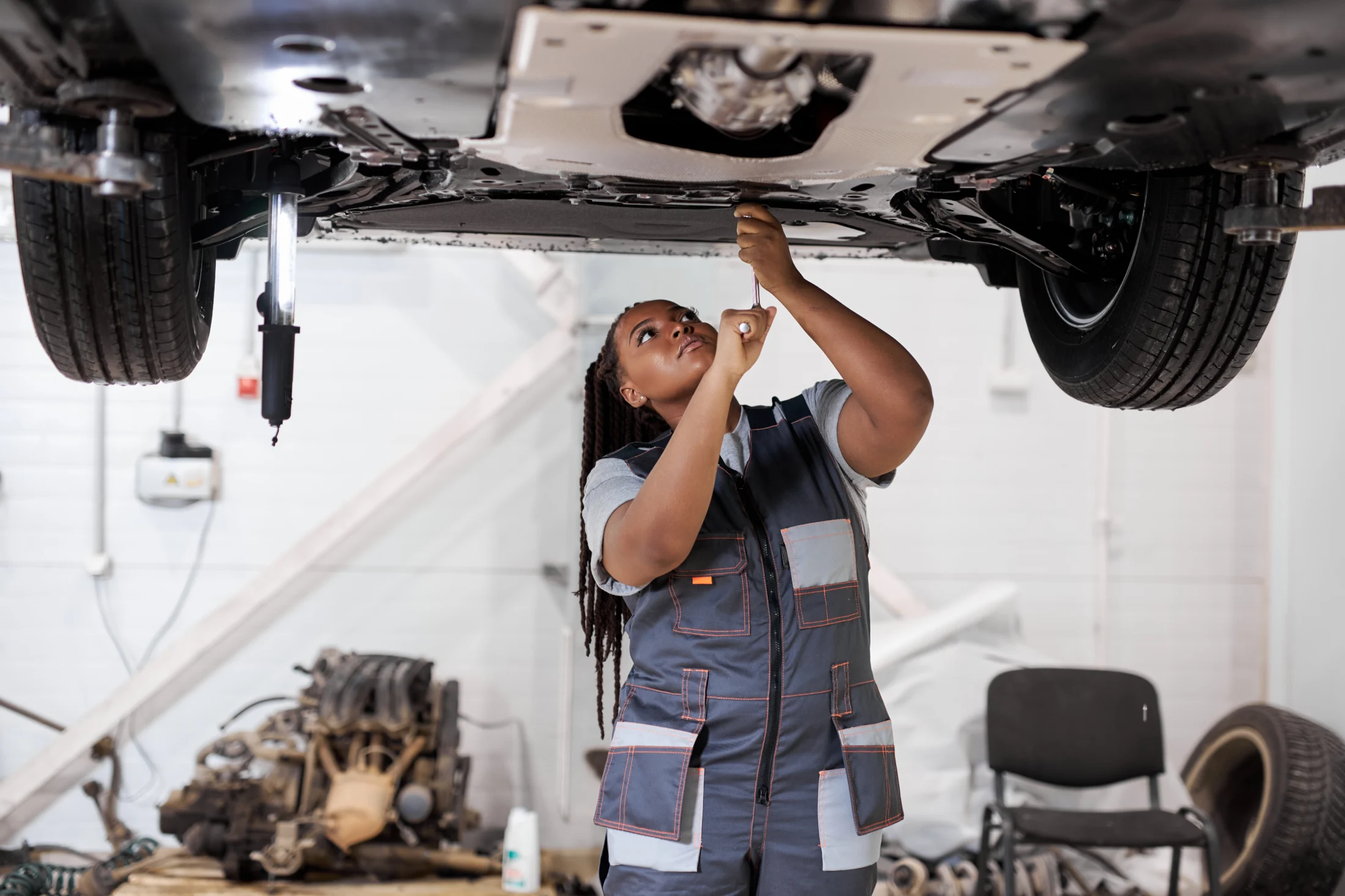 Mechanic in a uniform works attentively under a lifted car in a garage. The scene conveys focus and expertise in an automotive repair setting.