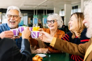Group of seniors sharing a cheerful toast around a cafe table with coffee and pastries