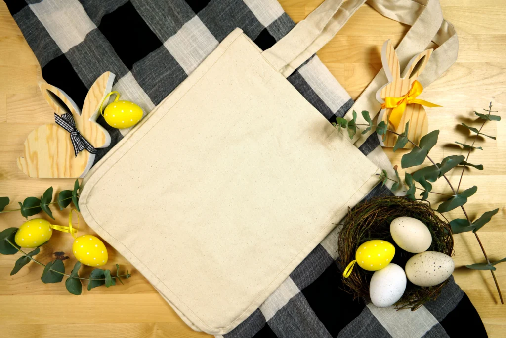 tote bags for Easter egg hunt laid out in a pile on wooden table surrounded by eggs, wooden bunnies and foliage
