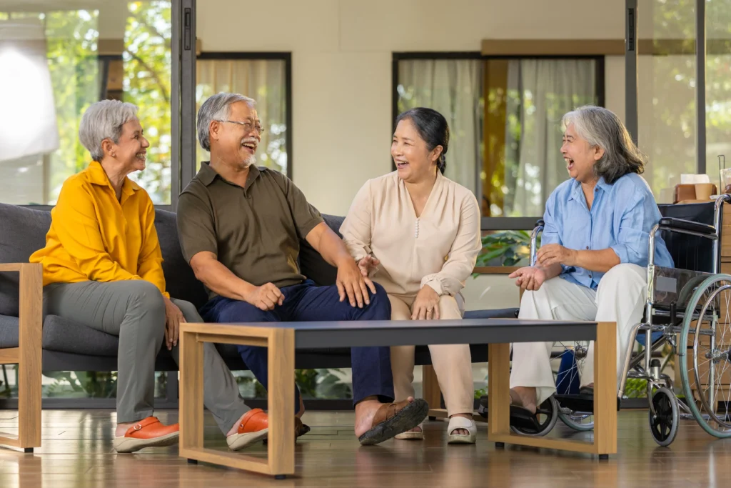 Group of four seniors laughing and chatting together with one on in a wheelchair and the rest on a couch