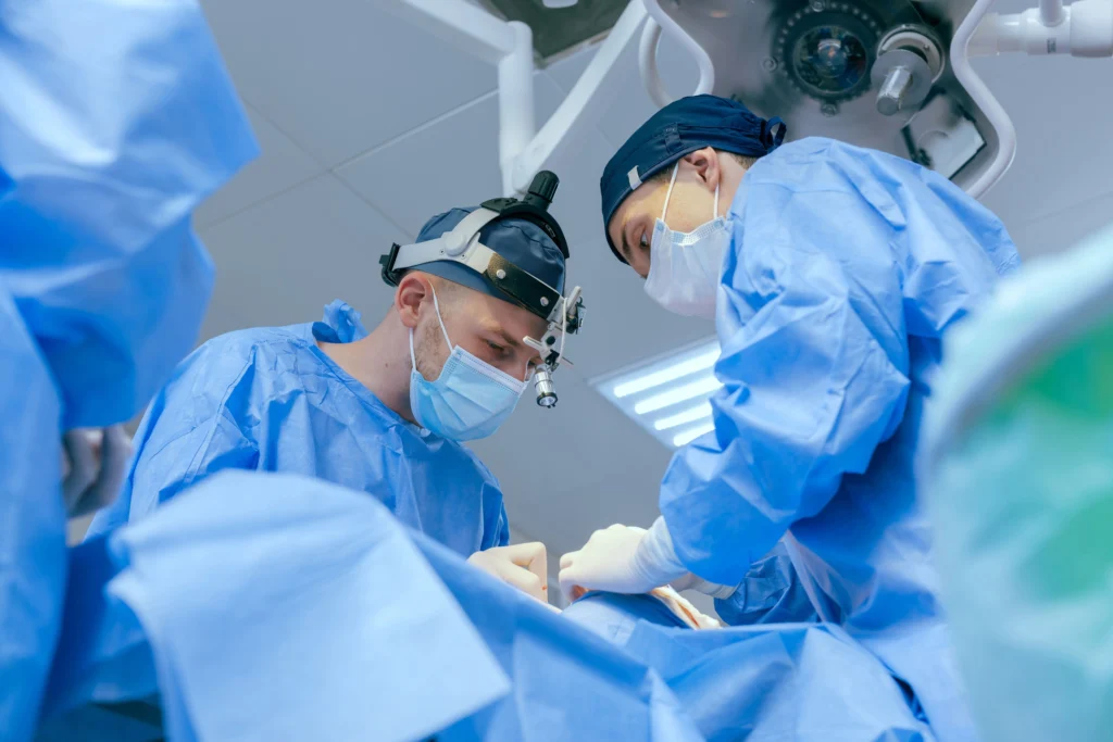 Two surgeons with surgical gowns, masks, and surgical equipment doing an elective surgery on patient with private health insurance hospital cover