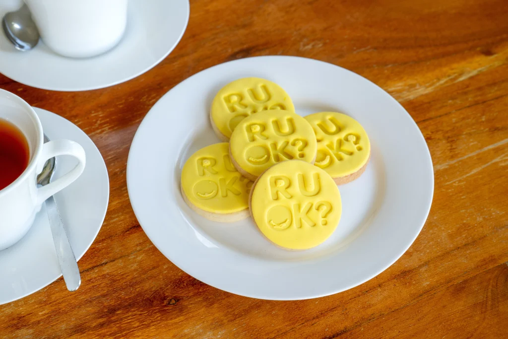 Yellow R U OK Day biscuits on a plate with cups of tea, ready for an R U OK Day morning tea