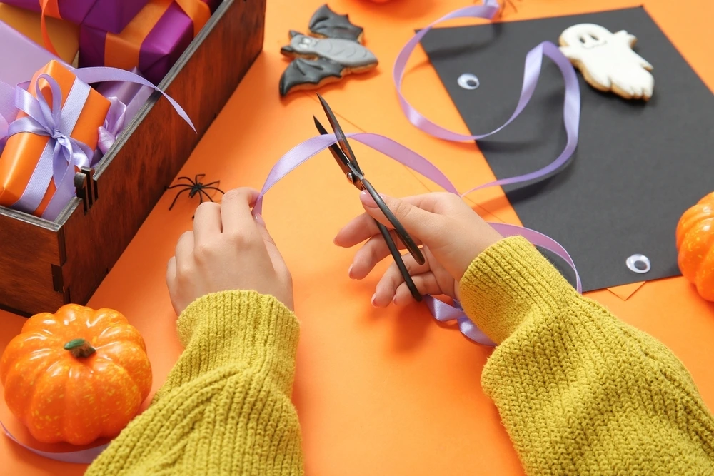Cutting ribbon at a halloween crafting station. Surrounded but orange pumkins, black paper and purple accessories.