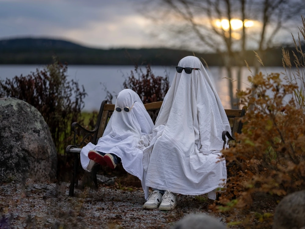 Two people wearing bed sheets over their head and added sunglasses to make them look like ghosts