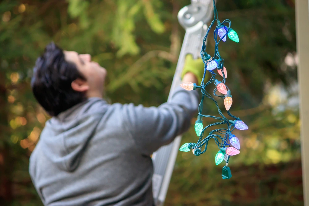 A handy man on a ladder, hanging up Christmas lights in his neighbourhood